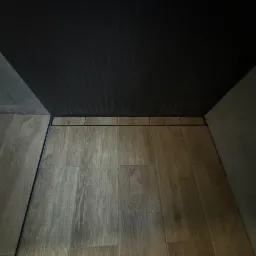 Ukończona podłoga w łazience z drewnopodobnych płytek ceramicznych i liniowym odpływem, widok z dołu, ciemny sufit z listwami.