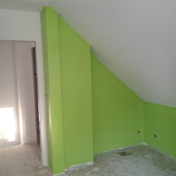 Adrian Lemke - Świeżo pomalowane na zielono poddasze ze skosami, widoczne ślady farby na podłodze i puszka z farbą w rogu.
