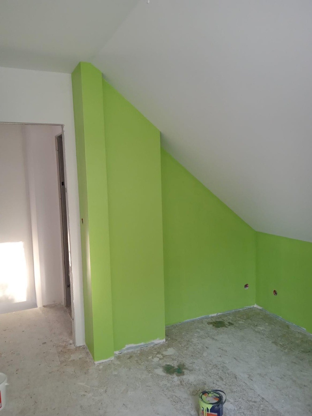 Świeżo pomalowane na zielono poddasze ze skosami, widoczne ślady farby na podłodze i puszka z farbą w rogu.