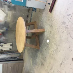 Okrągły stół z jasnego drewna, z oryginalną konstrukcją nóg, wykonany w Świdniku, widoczny w warsztacie podczas produkcji.