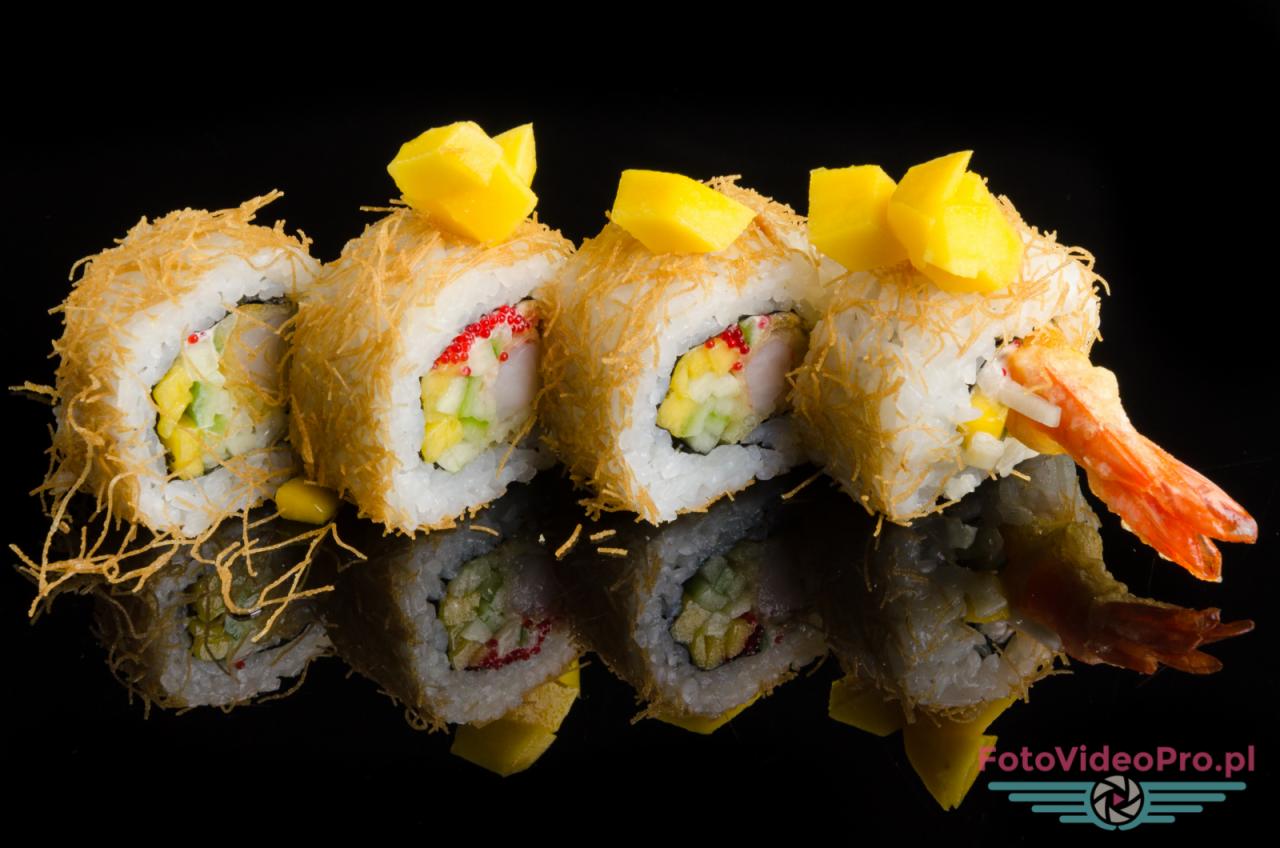 Cztery rolki sushi z mango, krewetką, ogórkiem i kawiorem tobiko, owinięte w cienki makaron sojowy, na czarnym, błyszczącym tle.