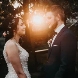 Para młoda wpatrzona w siebie podczas sesji w plenerze, w tle zachodzące słońce i zieleń drzew.