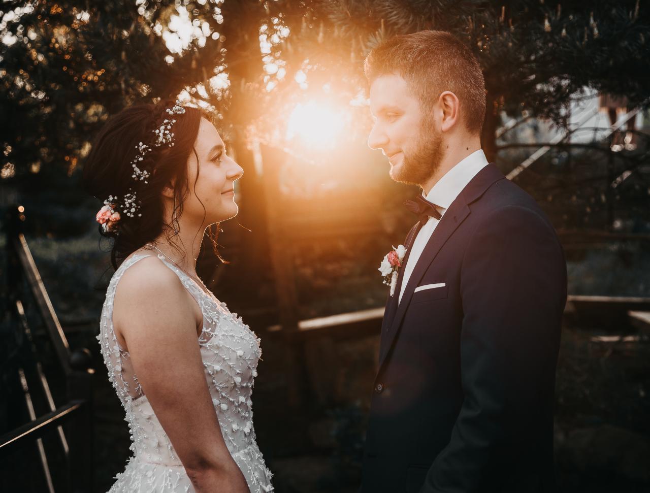 Para młoda wpatrzona w siebie podczas sesji w plenerze, w tle zachodzące słońce i zieleń drzew.