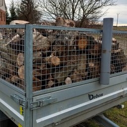 Zieleń i Drewno - Przyczepa marki Debon wypełniona pociętymi kawałkami drewna, widoczna na tle pola i drzew bez liści pod pochmurnym niebem.