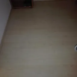 Jasne panele podłogowe ułożone wzdłuż ściany, widoczna listwa przypodłogowa i fragment szafki na buty w rogu pomieszczenia.