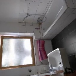 Wykończona łazienka z białymi i szarymi płytkami, drewnianą ramą okienną i wiszącym ręcznikiem w odcieniach różu i fioletu.