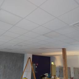 Budullux - Kasetonowy sufit podwieszany w jasnym pomieszczeniu, widoczna drabina i przygotowania do prac wykończeniowych ścian.