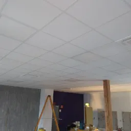 Kasetonowy sufit podwieszany w jasnym pomieszczeniu, widoczna drabina i przygotowania do prac wykończeniowych ścian.