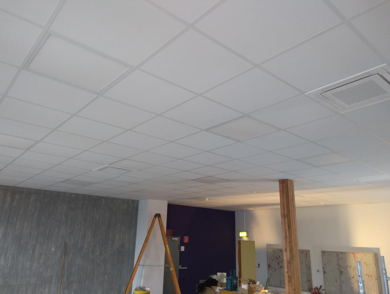 Kasetonowy sufit podwieszany w jasnym pomieszczeniu, widoczna drabina i przygotowania do prac wykończeniowych ścian.