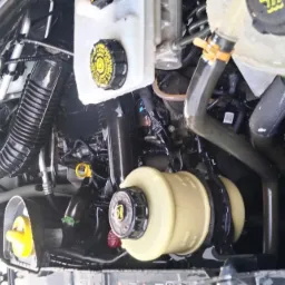 Wnętrze komory silnika samochodu, widoczne zbiorniki płynów eksploatacyjnych, przewody i elementy konstrukcyjne, po umyciu, z widocznymi kroplami wody.