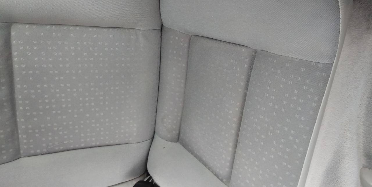 Jasnoszara tapicerka samochodowa z delikatnym wzorem w kropki, widoczne szwy i załamania materiału, lekko przybrudzona w dolnej części.