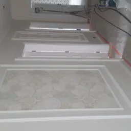 Korytarz w trakcie wykańczania z panelami dekoracyjnymi z tapetą w okrągłe wzory, białe listwy przypodłogowe i ościeżnice, widoczne przewody elektryczne i drabina w tle.