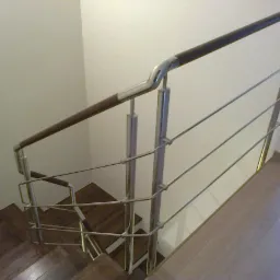 Schody z ciemnego drewna z balustradą ze stali nierdzewnej z drewnianym poręczą, widok z góry, jasne ściany i podłoga.