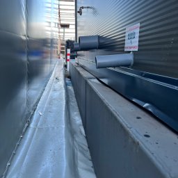 MGO Mateusz Gosz - Przyłącze elektryczne tymczasowe na placu budowy, widoczne rury i przewody wzdłuż ściany kontenera, zabezpieczone przed warunkami atmosferycznymi.