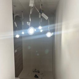 MGO Mateusz Gosz - Nowoczesne oświetlenie LED w łazience w trakcie montażu, widoczne przewody i zasilacze. Jasne światło punktowe. Częściowo widoczna toaleta i surowe wykończenie.