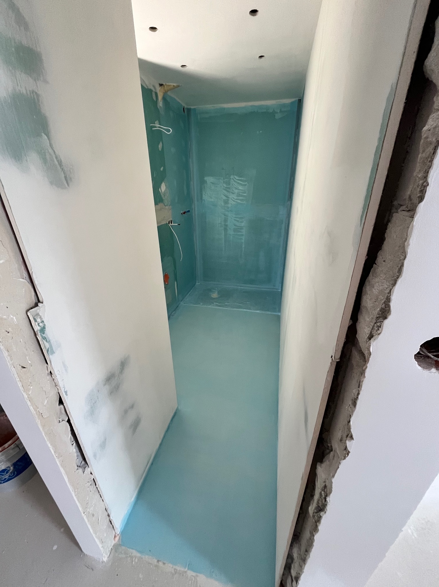 Wnętrze łazienki w trakcie remontu. Widoczne płyty karton-gips na ścianach, przygotowane do szpachlowania. Podłoga zabezpieczona folią. Przewody elektryczne.