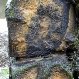 Fragment kamiennej kolumny z widocznymi śladami napraw i konserwacji, z zaciekami i mchem, ukazujący strukturę i teksturę kamienia.
