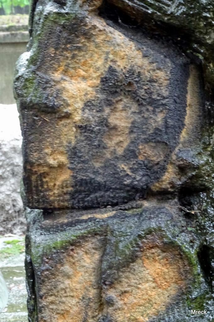 Fragment kamiennej kolumny z widocznymi śladami napraw i konserwacji, z zaciekami i mchem, ukazujący strukturę i teksturę kamienia.