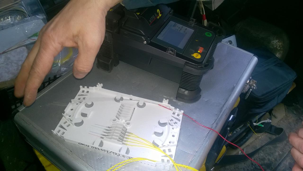 Spawarka światłowodowa S178A2 na metalowej walizce z kasetą światłowodową i włóknami światłowodowymi w kolorach żółtym i czerwonym, widoczna dłoń operatora.