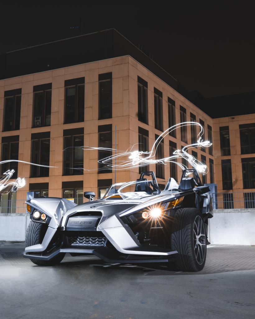 Trzykołowy pojazd Polaris Slingshot w nocnej scenerii miejskiej z efektami świetlnymi