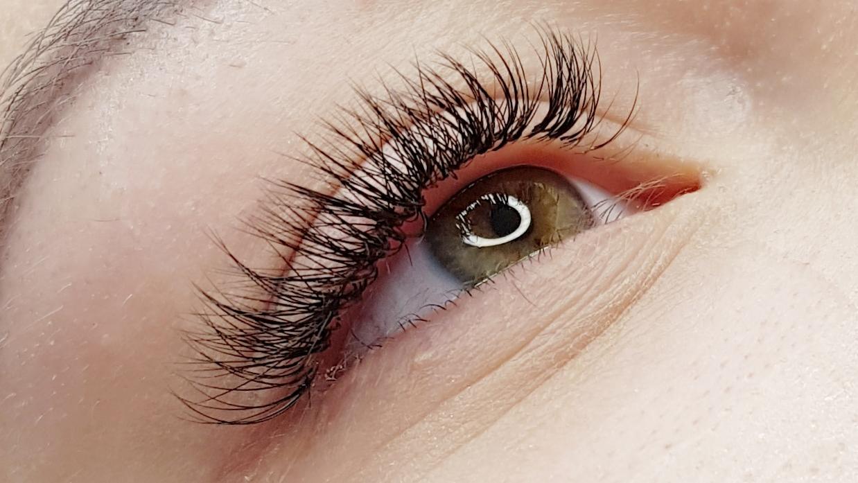Zbliżenie na oko z długimi, gęstymi, czarnymi rzęsami po zabiegu przedłużania, widoczna delikatna skóra powiek i brwi.