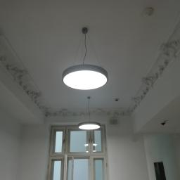 6th Avenue - Białe wnętrze z dekoracyjnym sufitem, dwoma okrągłymi lampami wiszącymi i oknem balkonowym z ozdobną balustradą na zewnątrz.