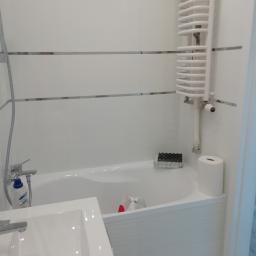 6th Avenue - Biała łazienka z wanną obudowaną panelami, grzejnikiem drabinkowym i umywalką z baterią, widoczny środek czyszczący Sidolux.