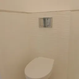 Podwieszana toaleta z białym siedziskiem i chromowanym przyciskiem spłukującym na ścianie z dekoracyjnymi, falistymi płytkami w minimalistycznej, jasnej łazience.