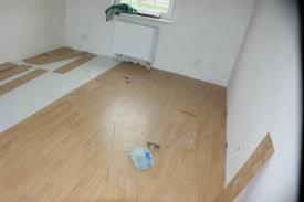 Układanie paneli podłogowych w pokoju, widoczne panele przed montażem, częściowo ułożona podłoga, grzejnik pod oknem, niebieska ścierka na podłodze.