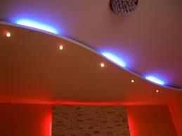 Sufit podwieszany z oświetleniem LED w kolorach niebieskim i czerwonym, dekoracyjna listwa sufitowa, widoczny fragment żyrandola.