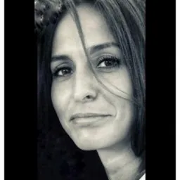 Portret kobiety o ciemnych włosach, z delikatnym uśmiechem, w czarno-białej tonacji, z włosami opadającymi na twarz.