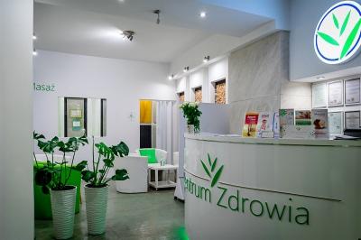 Jasne wnętrze recepcji centrum zdrowia z roślinami doniczkowymi, białym biurkiem z logo i dyplomami na ścianie