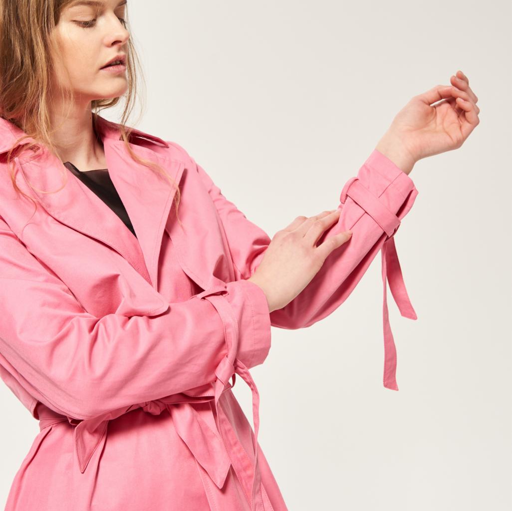 Kobieta w różowym trenczu z podwiniętymi rękawami, prezentująca detal wiązania na mankiecie.