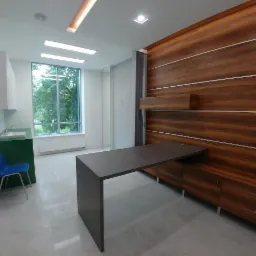 Nowoczesne wnętrze z blatem zintegrowanym z szafkami z drewnopodobnej płyty, po lewej stronie zielona szafka z umywalką i niebieskie krzesło.