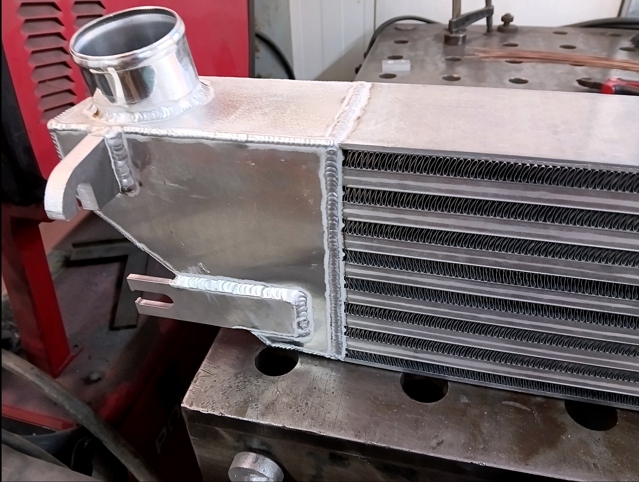 Aluminiowy intercooler samochodowy po spawaniu TIG, widoczne spoiny na metalowej konstrukcji. Detal na stole warsztatowym.
