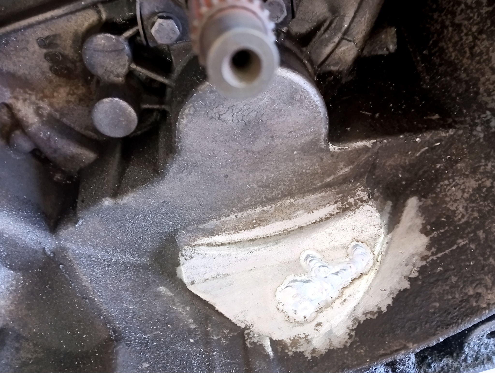 Szczegółowe ujęcie spawu na metalowej konstrukcji, z widocznymi śladami obróbki i elementami mocującymi. Surowy, techniczny charakter.