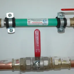 Instalacja wodna z odkamieniaczem Limetron 1/2, widoczne miedziane i zielone rury połączone złączkami i zaworami, zamontowane na białej ścianie.