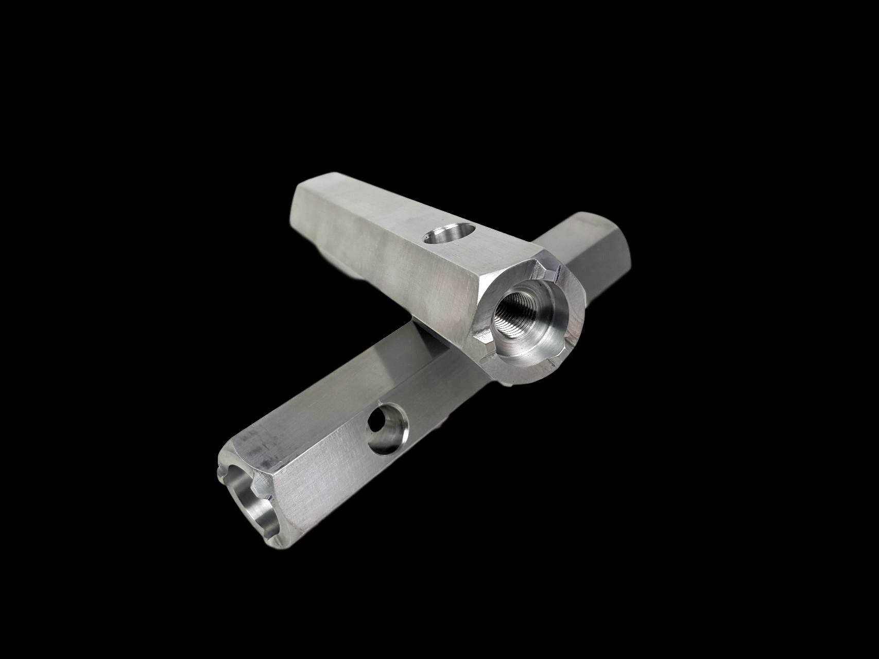 Dwa metalowe, sześciokątne pręty z otworami, jeden z gwintem wewnętrznym, leżące na czarnym tle z delikatnym odbiciem.