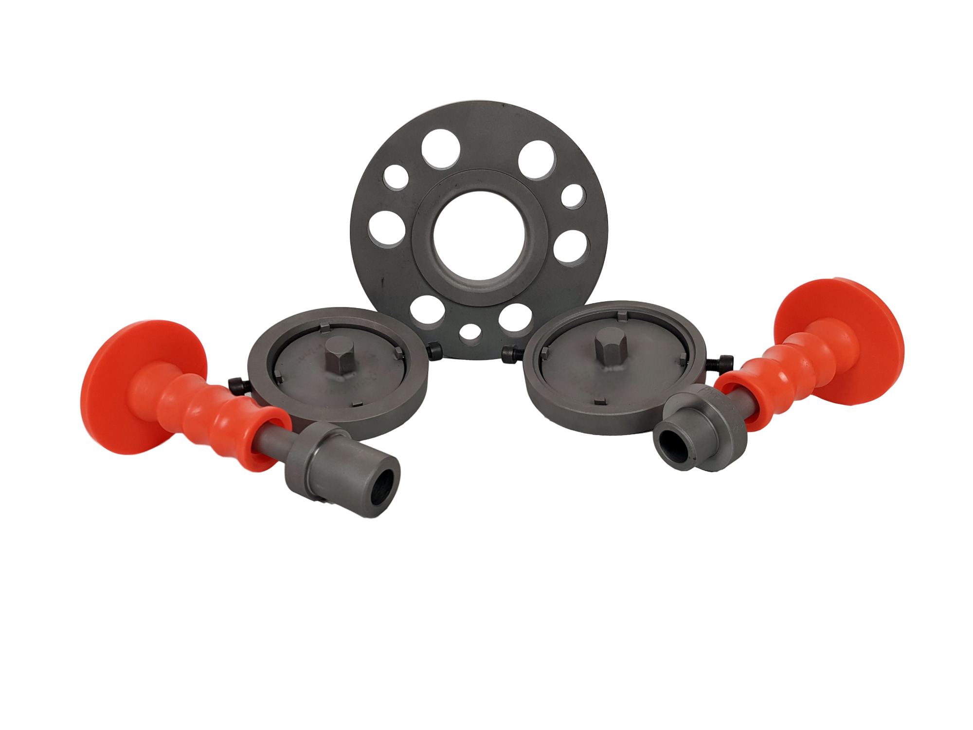 Zestaw przyrządów montażowych: okrągła tarcza z otworami i dwa uchwyty z czerwonymi rękojeściami, leżące na białym tle.