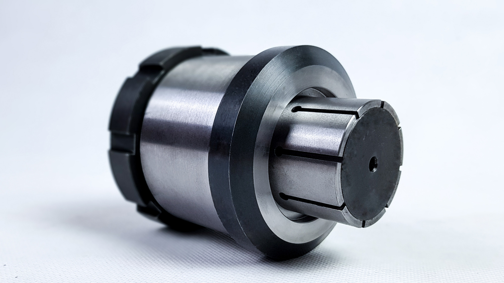 Precyzyjny uchwyt tokarski ER na białym tle, widoczne nacięcia i otwór centralny, metal o satynowym wykończeniu, czarne gumowe pierścienie.