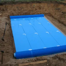 Niebieska izolacja termiczna z rurami drenażowymi ułożona w wykopie, przygotowana do zasypania ziemią.