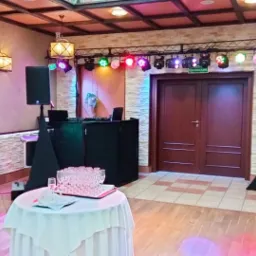 Sala bankietowa przygotowana na imprezę z nagłośnieniem, oświetleniem scenicznym i stołem z kieliszkami.