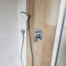 Nowoczesna kabina prysznicowa z chromowaną armaturą i panelami imitującymi drewno, kontrastująca z jasnymi płytkami.