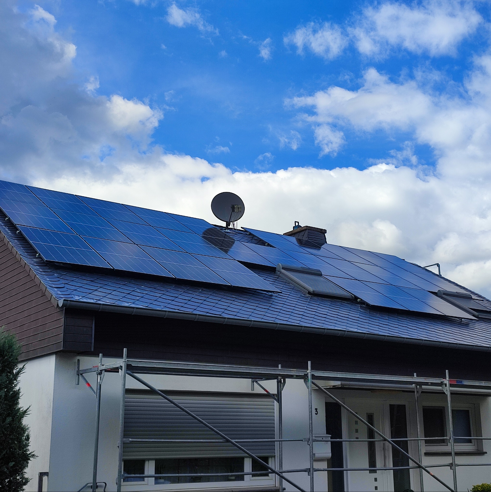 Dom z panelami słonecznymi na dachu, widoczna antena satelitarna, rusztowanie przed budynkiem.