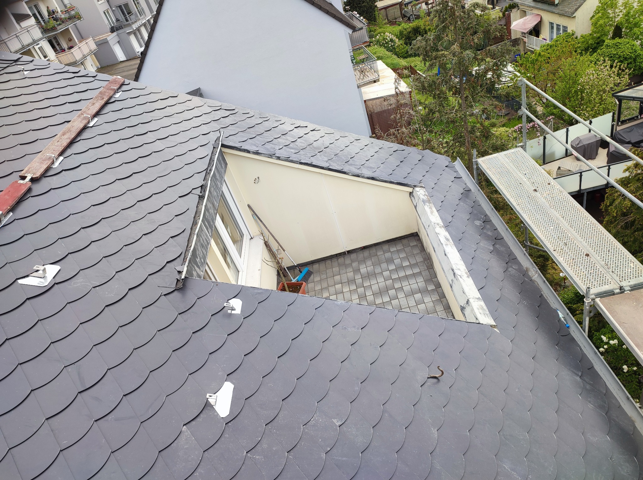 Fragment dachu pokrytego łupkiem z otwartym oknem dachowym, widoczne rusztowanie i elementy mocujące łatę dachową.