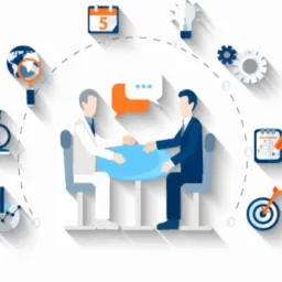 Grafika przedstawiająca dwóch mężczyzn siedzących przy okrągłym, niebieskim stole, otoczonych ikonami symbolizującymi analizę danych, globalny zasięg, innowacje, planowanie i cel. Widoczne ikony to...