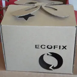 Kartonowe pudełko prezentowe z wyciętym logo ECOFIX i symbolem recyklingu, ozdobione kokardą z tektury falistej.