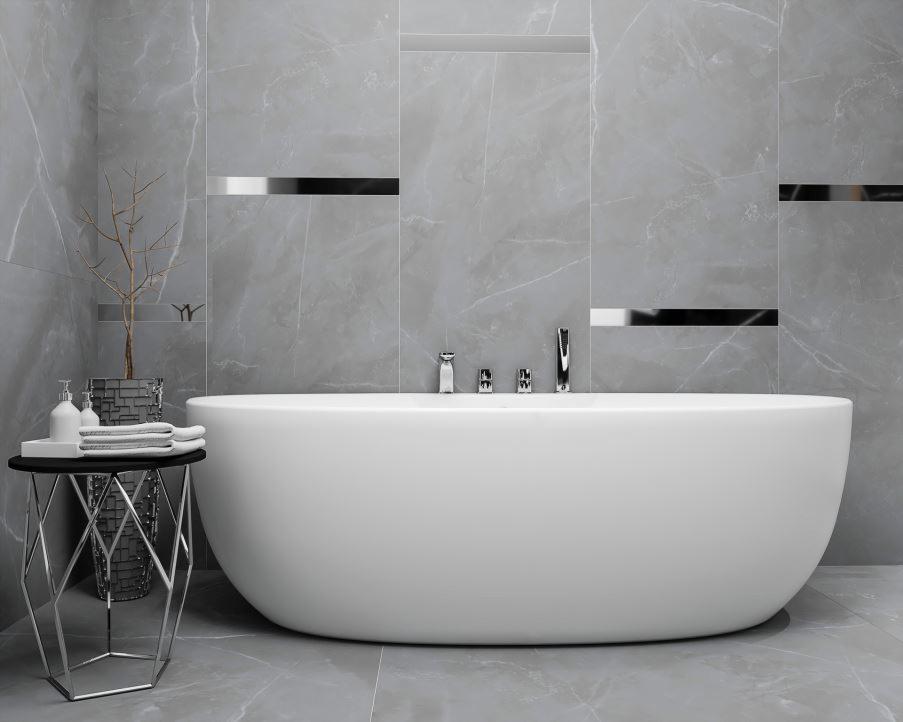 Nowoczesna łazienka z wolnostojącą białą wanną na tle szarych marmurowych płytek z metalowymi akcentami, uzupełniona stolikiem pomocniczym z ręcznikami i minimalistyczną dekoracją z gałązek.