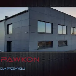 Zewnętrzny widok nowo wybudowanej, szarej hali przemysłowej z widocznymi oknami i drzwiami, z logo firmy SPAWKON w dolnej części kadru.