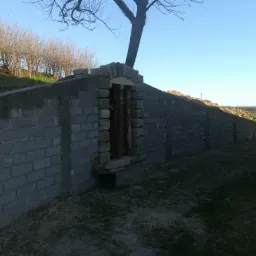 Częściowo ukończona murowana piwnica ziemianka z kamiennym łukiem nad wejściem, widoczna z zewnątrz, na tle zieleni i błękitnego nieba.